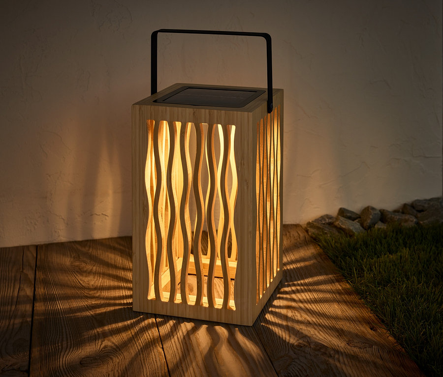 Lampion solarny stoi na drewnianej podłodze i rzuca cień.