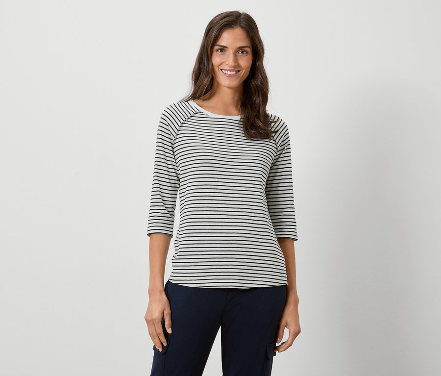 Kobieta ma na sobie bluzkę w paski z długim rękawem i granatowe spodnie na białym tle.