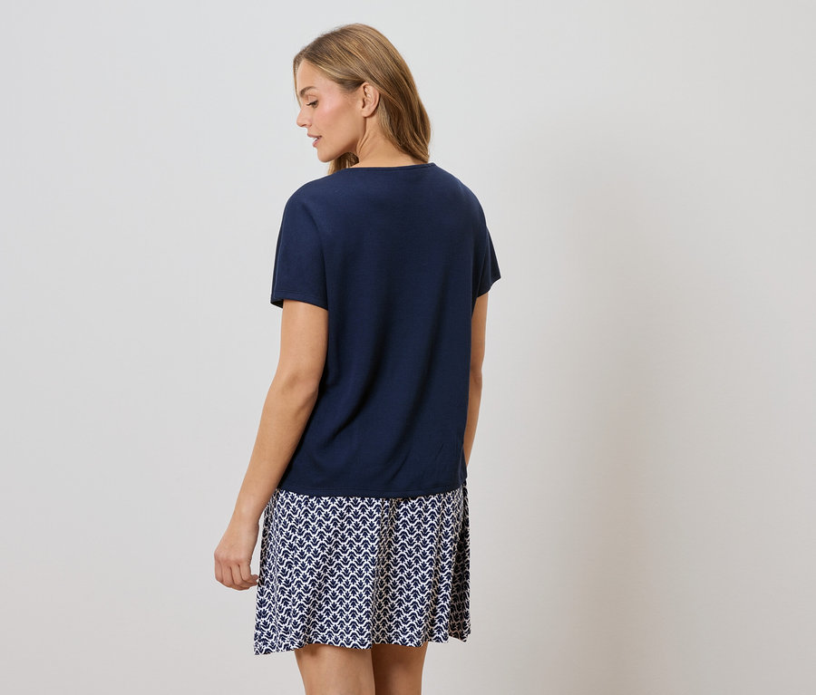 Widok z tyłu kobiety z blond włosami, ubranej w granatowy T-shirt i spódnicę w niebiesko-biały wzór.