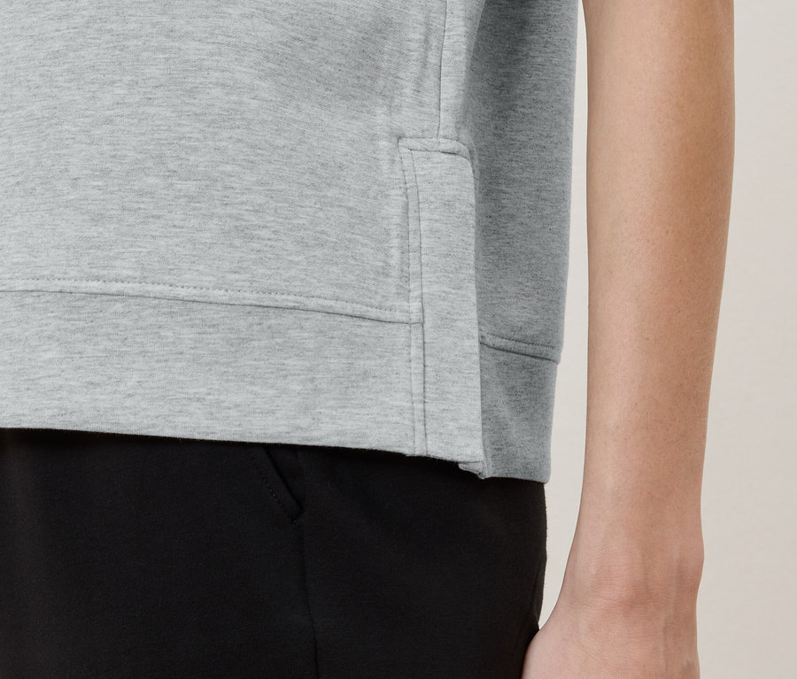 Szczegółowy widok osoby ubranej w jasno szary sweter i czarne spodnie.