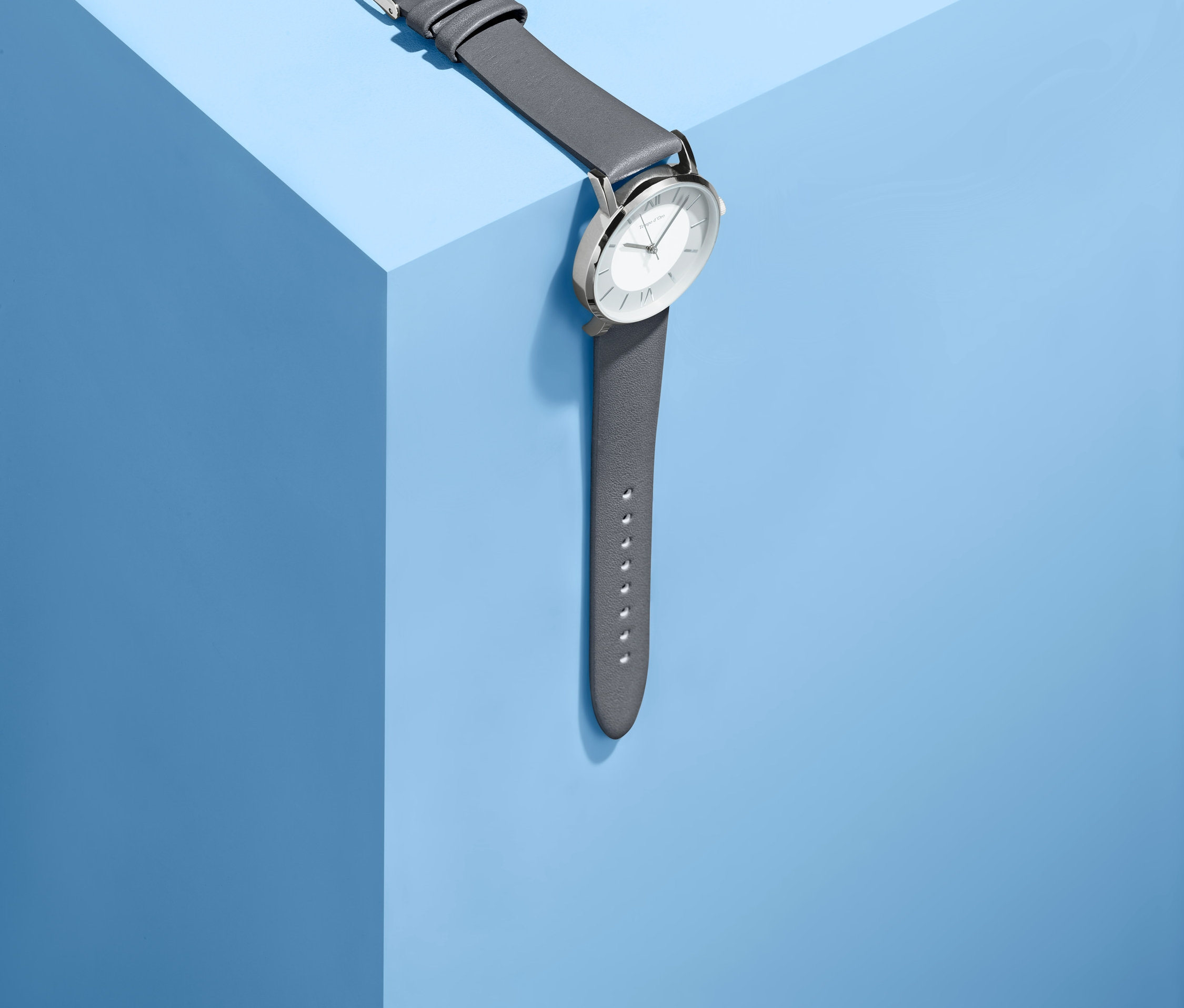 Zegarek damski ze skórzanym, szarym paskiem leży na niebieskiej powierzchni.