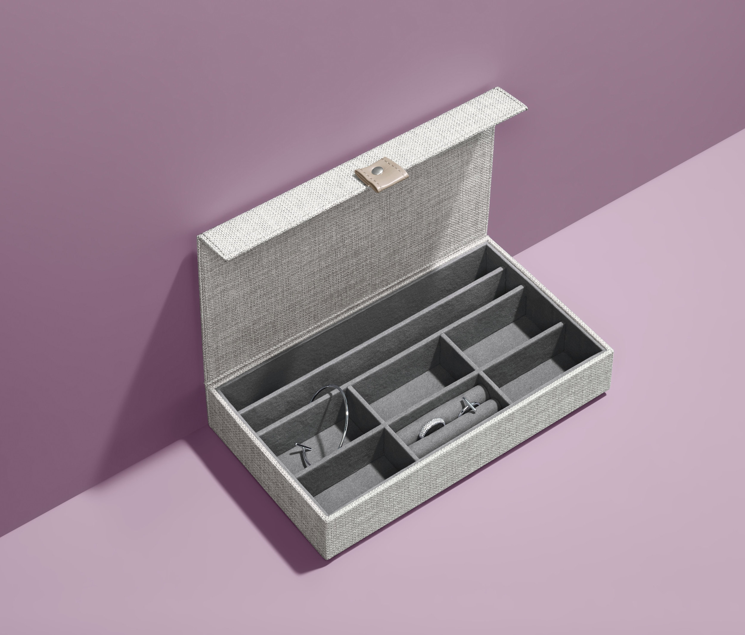 Otwarta szara kasetka na biżuterię z biżuterią na fioletowym tle.