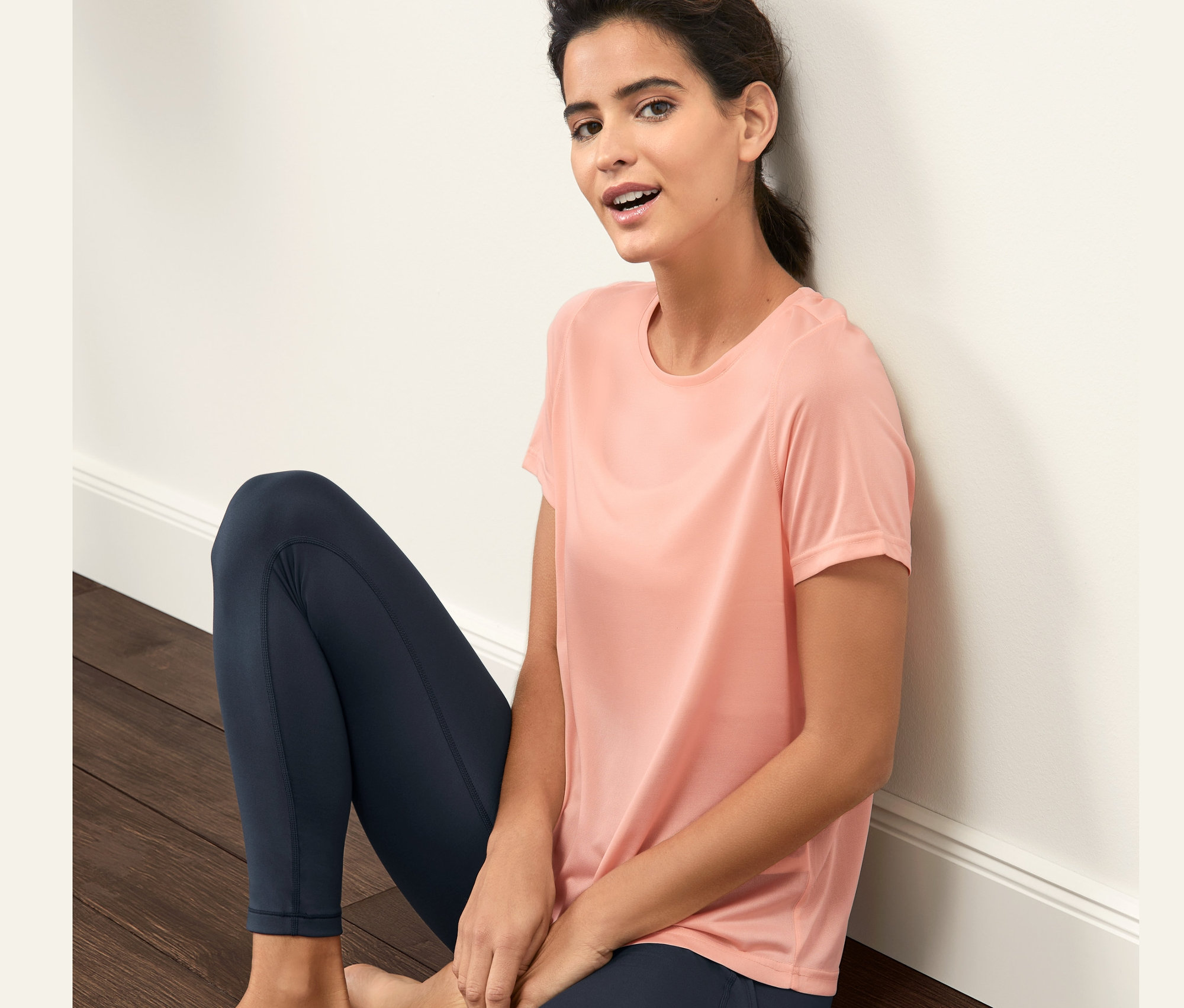 Kobieta siedzi na podłodze w koszulce sportowej.