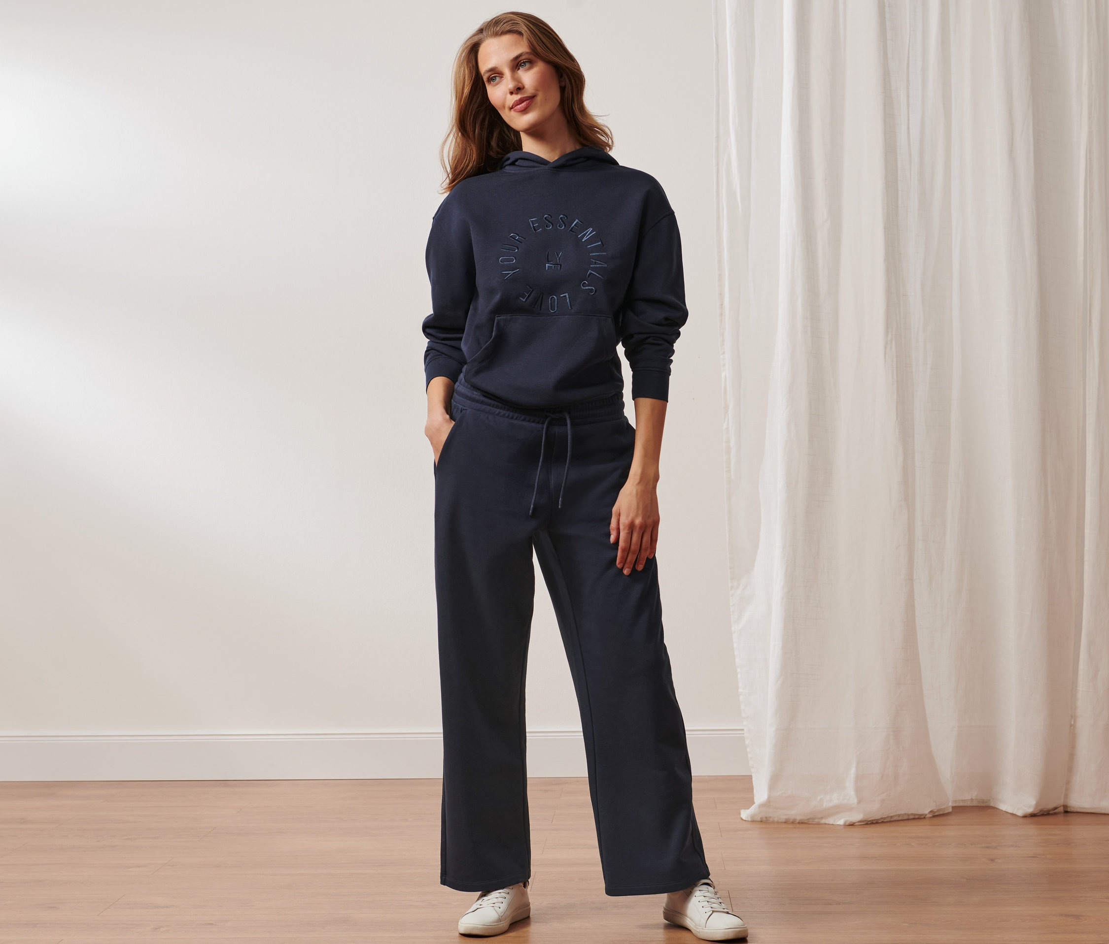 Kobieta stoi i pozuje w granatowej bluzie z kapturem i spodniach dresowych.