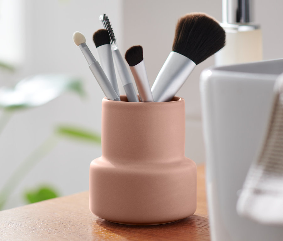 Różowy organizer z pędzlami do makijażu na drewnianej szafce.