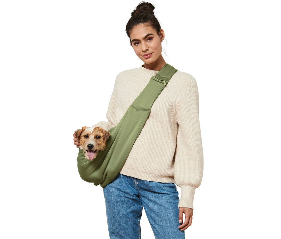 Kobieta z brązowym psem w zielonej torbie do transportu zwierząt.