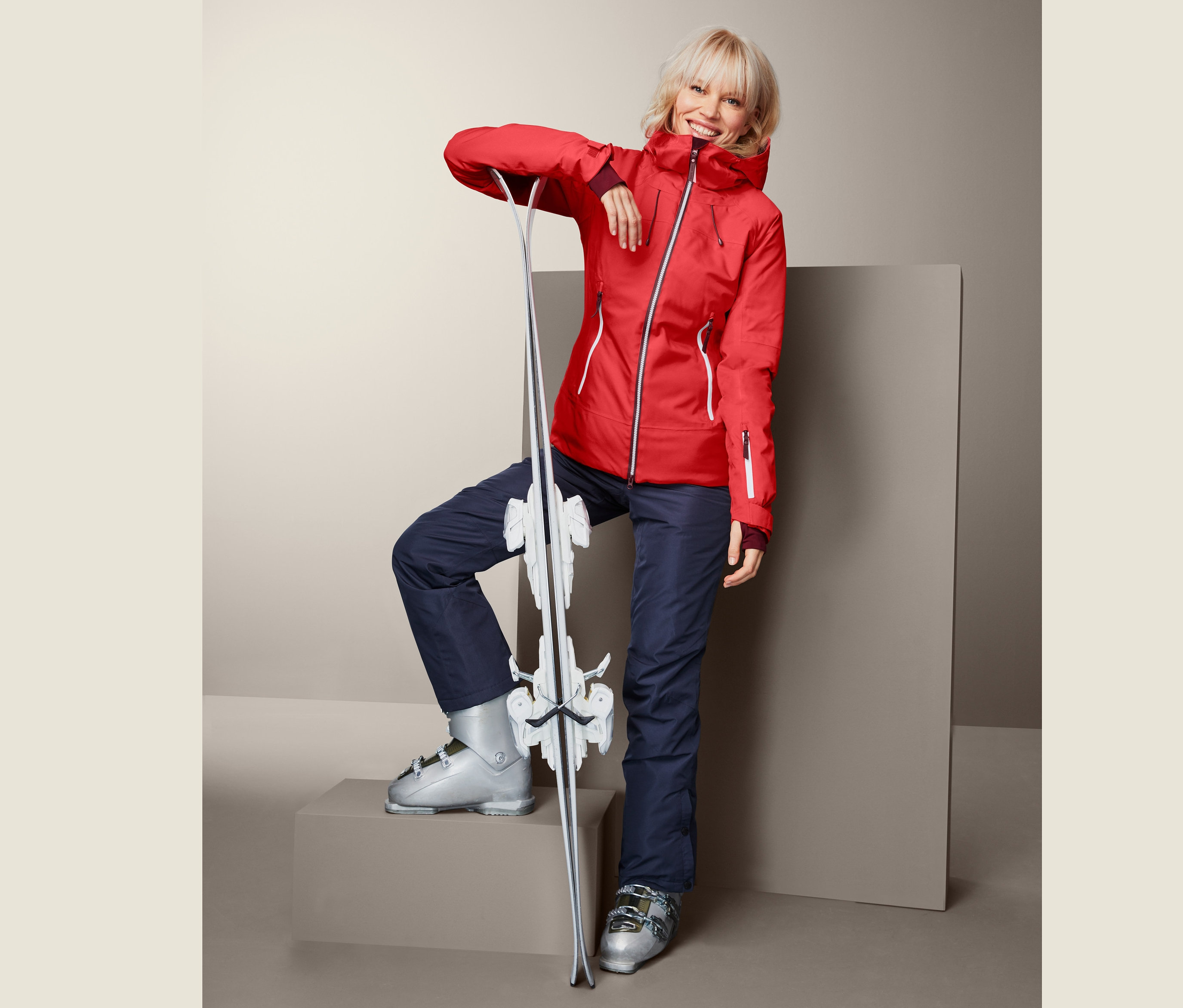 Kobieta w czerwonej damskiej kurtce narciarskiej opiera się o narty.