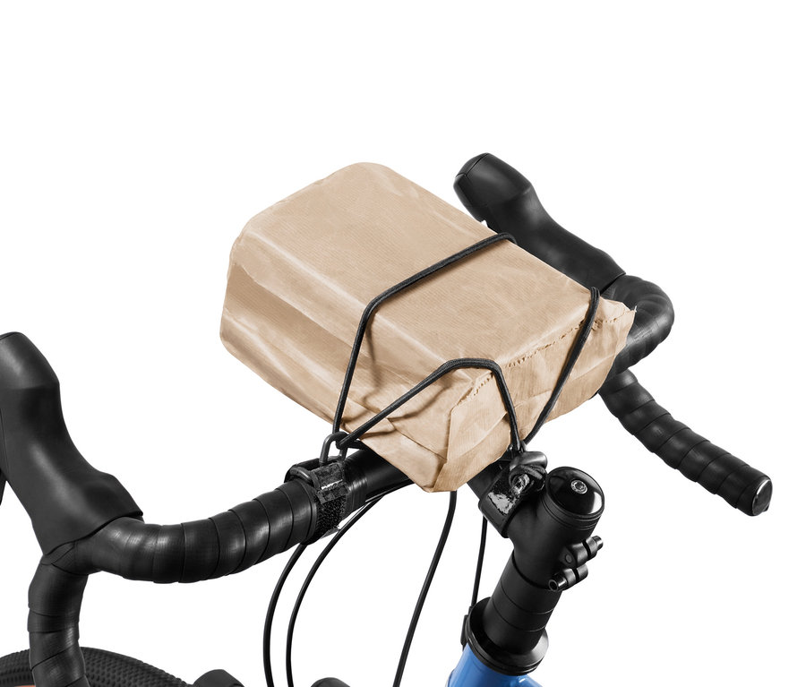 Brązowa papierowa torba przymocowana do kierownicy roweru za pomocą taśmy elastycznej.