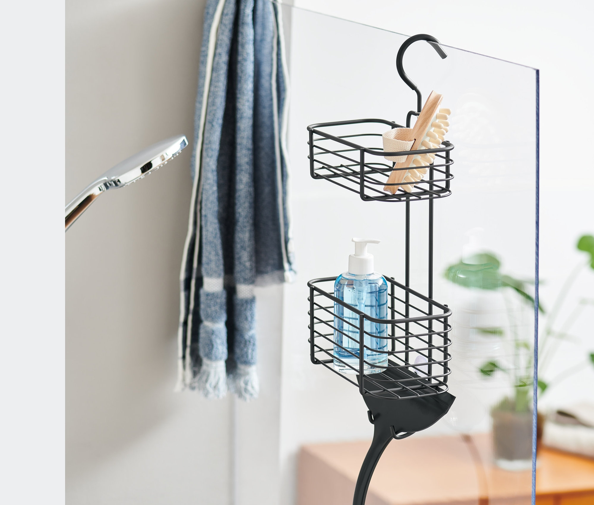 Czarny regał prysznicowy do powieszenia z szczotką, mydłem i ściągaczką wisi na szklanej ściance prysznicowej.