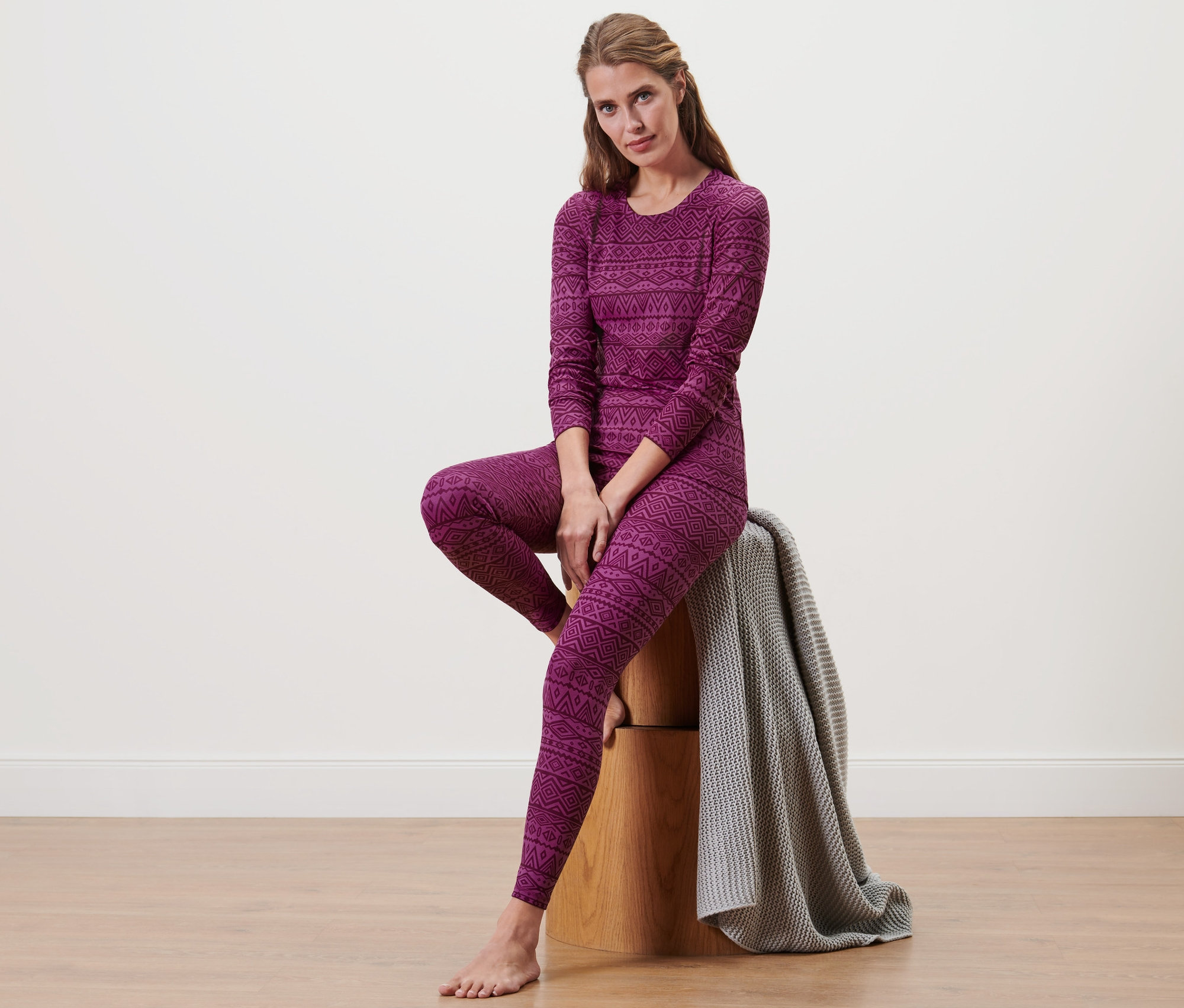 Kobieta siedzi na drewnianym stołku, ubrana w termoaktywną bieliznę funkcyjną.