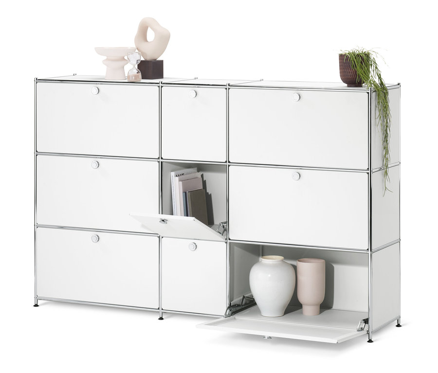 Biała komoda »CN3« z 9 klapami, z których jedna jest otwarta, z książkami i dekoracjami.