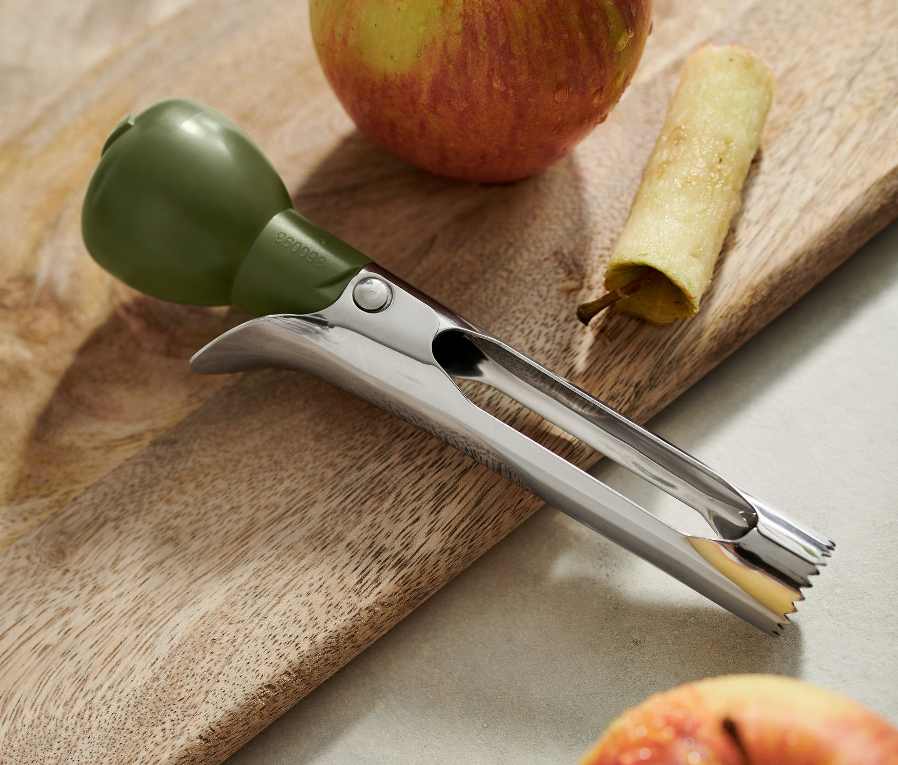 Drylownica do jabłek leży na drewnianej desce obok dwóch jabłek, z których jedno ma usunięty środek.