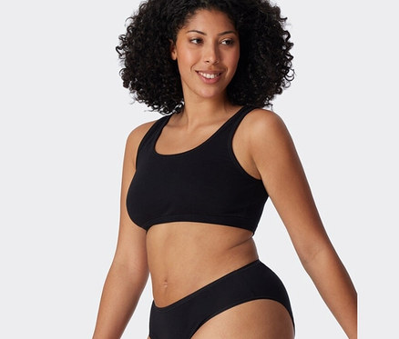 Kobieta ma na sobie czarny bralet z bawełny ekologicznej SCHIESSER z dwuczęściowego zestawu.