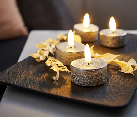 Cztery srebrne świeczki typu tea light LED z prawdziwego wosku na czarnej podkładce, ozdobione suszonymi kwiatami.