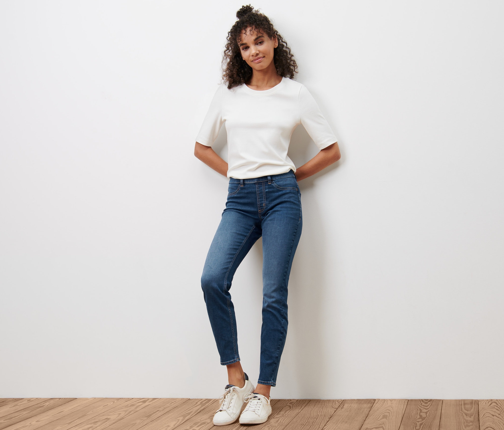 Kobieta pozuje na drewnianej podłodze w niebieskich tregginsach »Fit Nelly« i białym T-shircie.