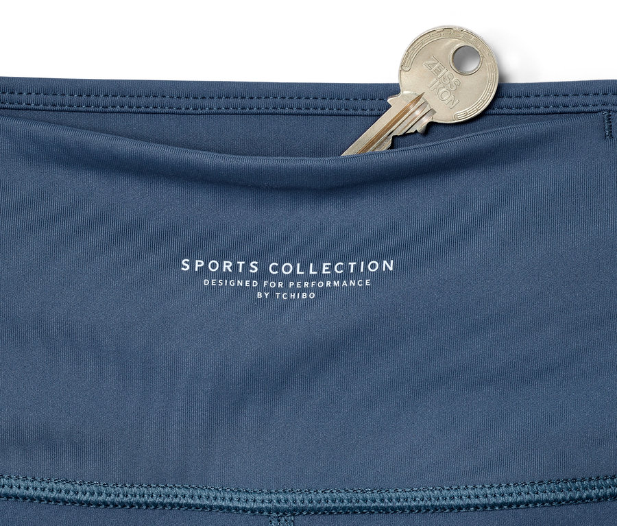 Szczegół niebieskich legginsów sportowych 7/8 z srebrnym kluczem w kieszeni.