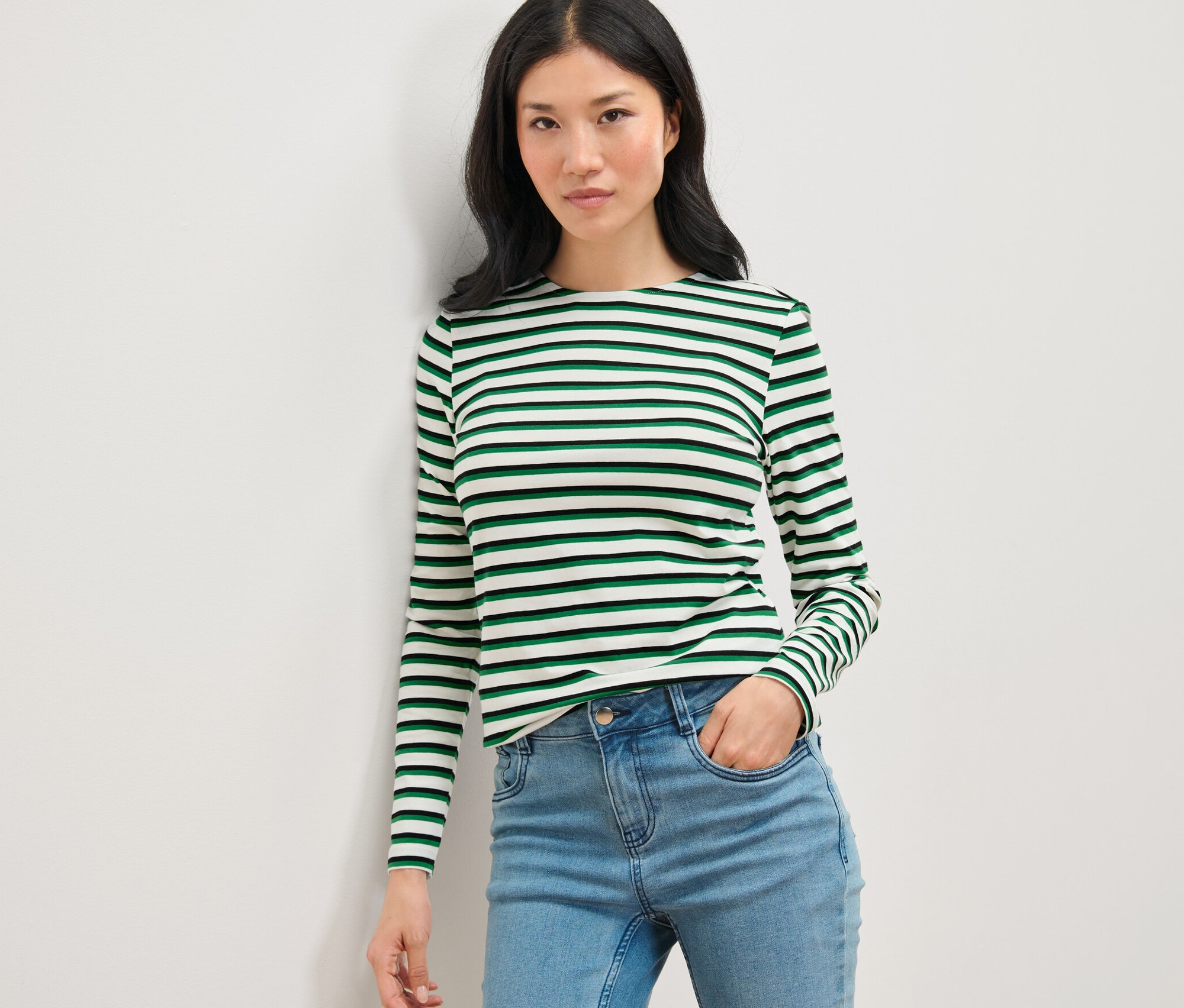 Kobieta pozuje w pasiastym, kolorowym longsleevie i dżinsach.