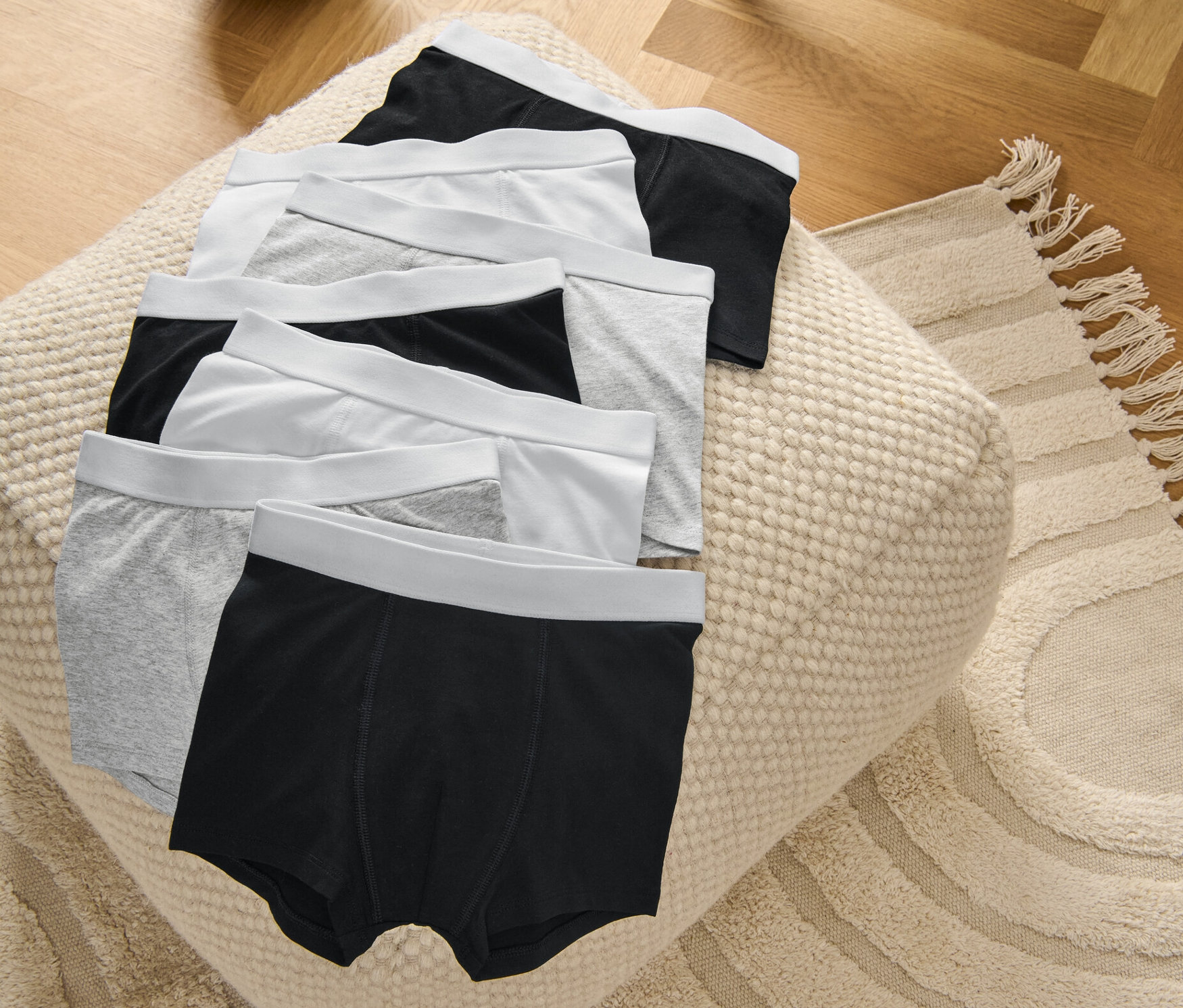 Na pufie leżą bokserki dziecięce, 7 par, szare, białe i czarne.