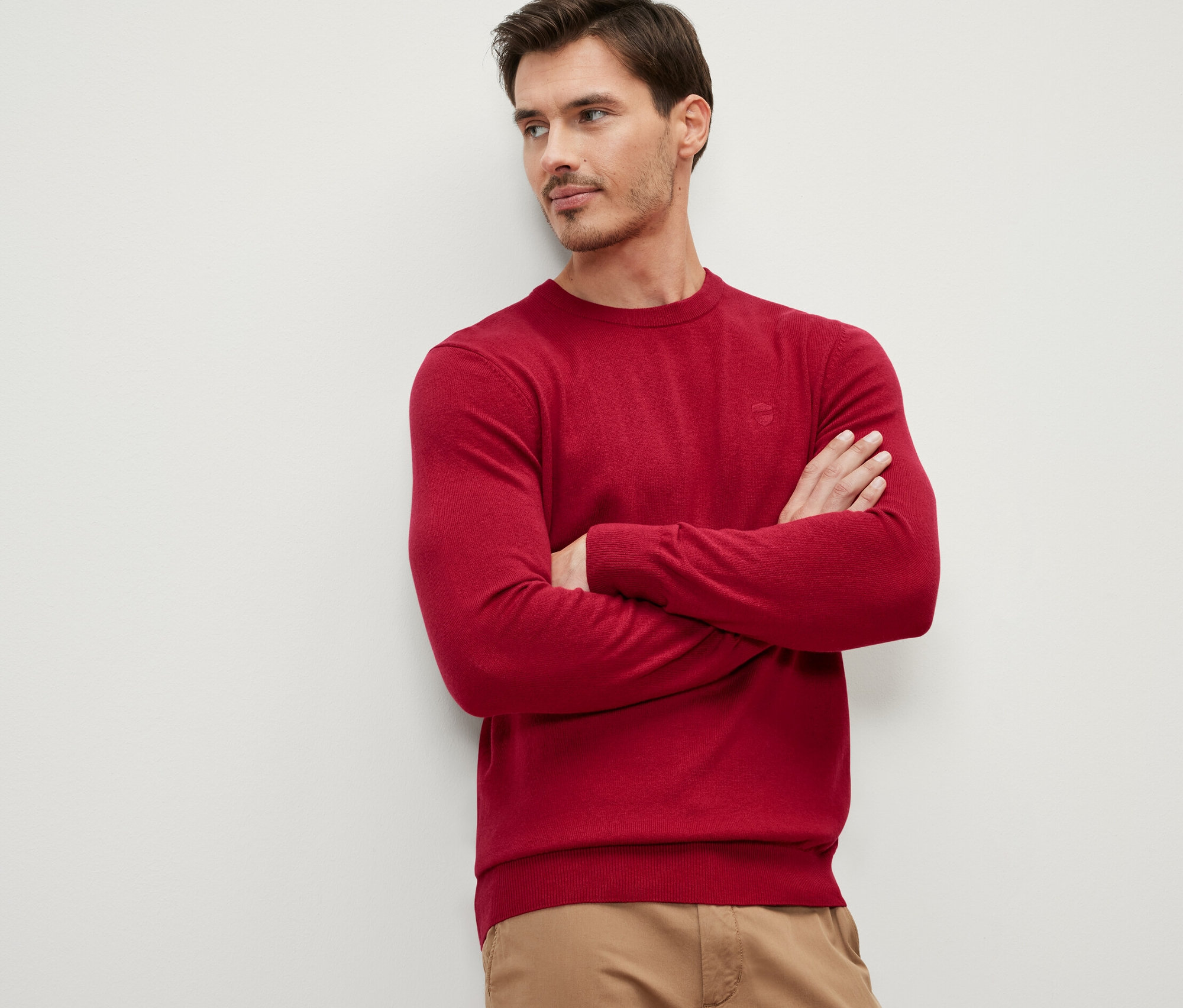 Mężczyzna ze skrzyżowanymi rękami na piersiach ma na sobie czerwony sweter z okrągłym dekoltem.