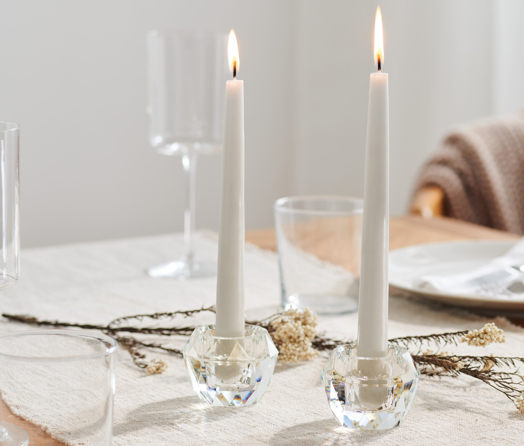 Dwa szklane świeczniki ze świecami na stole.