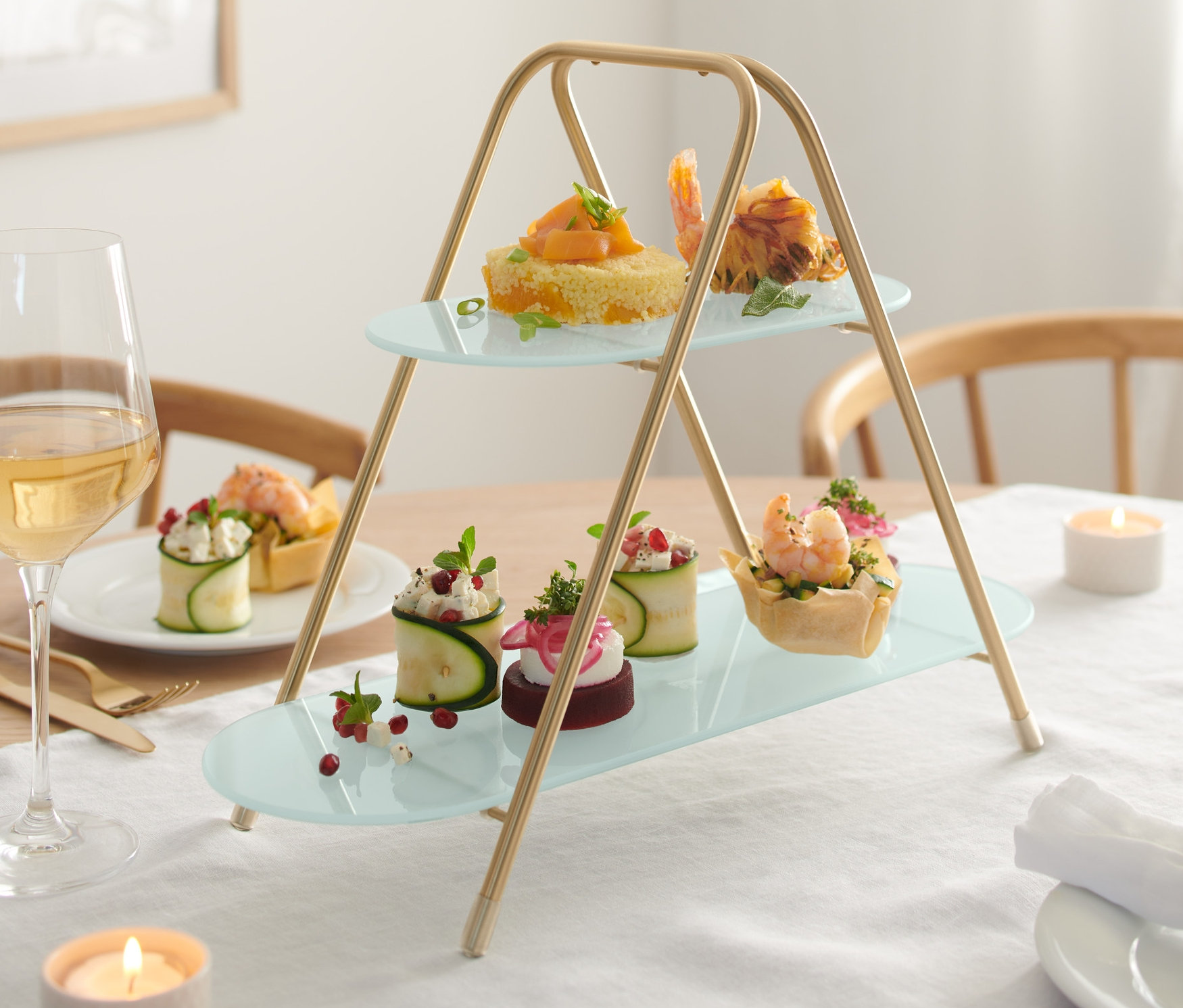 Dwupiętrowa etażerka z różnymi przekąskami na odświętnie nakrytym stole.