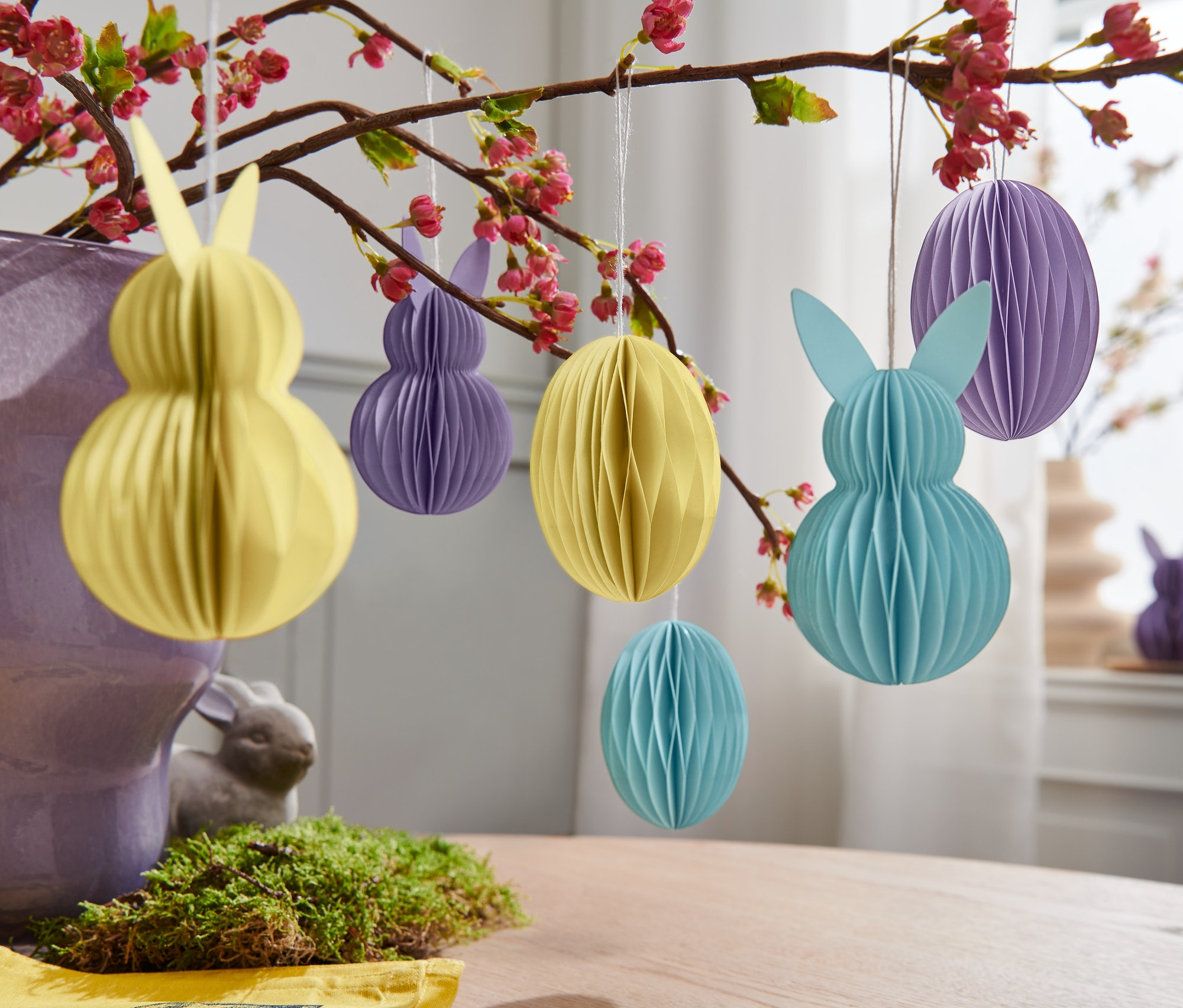 Żółte, fioletowe i niebieskie 6 papierowych zawieszek wielkanocnych wiszących na kwitnącej gałęzi.