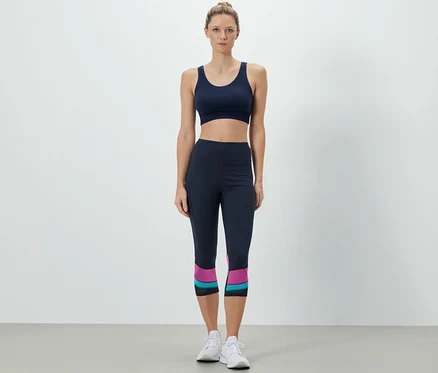 Kobieta ma na sobie biustonosz sportowy i legginsy sportowe o długości 3/4.