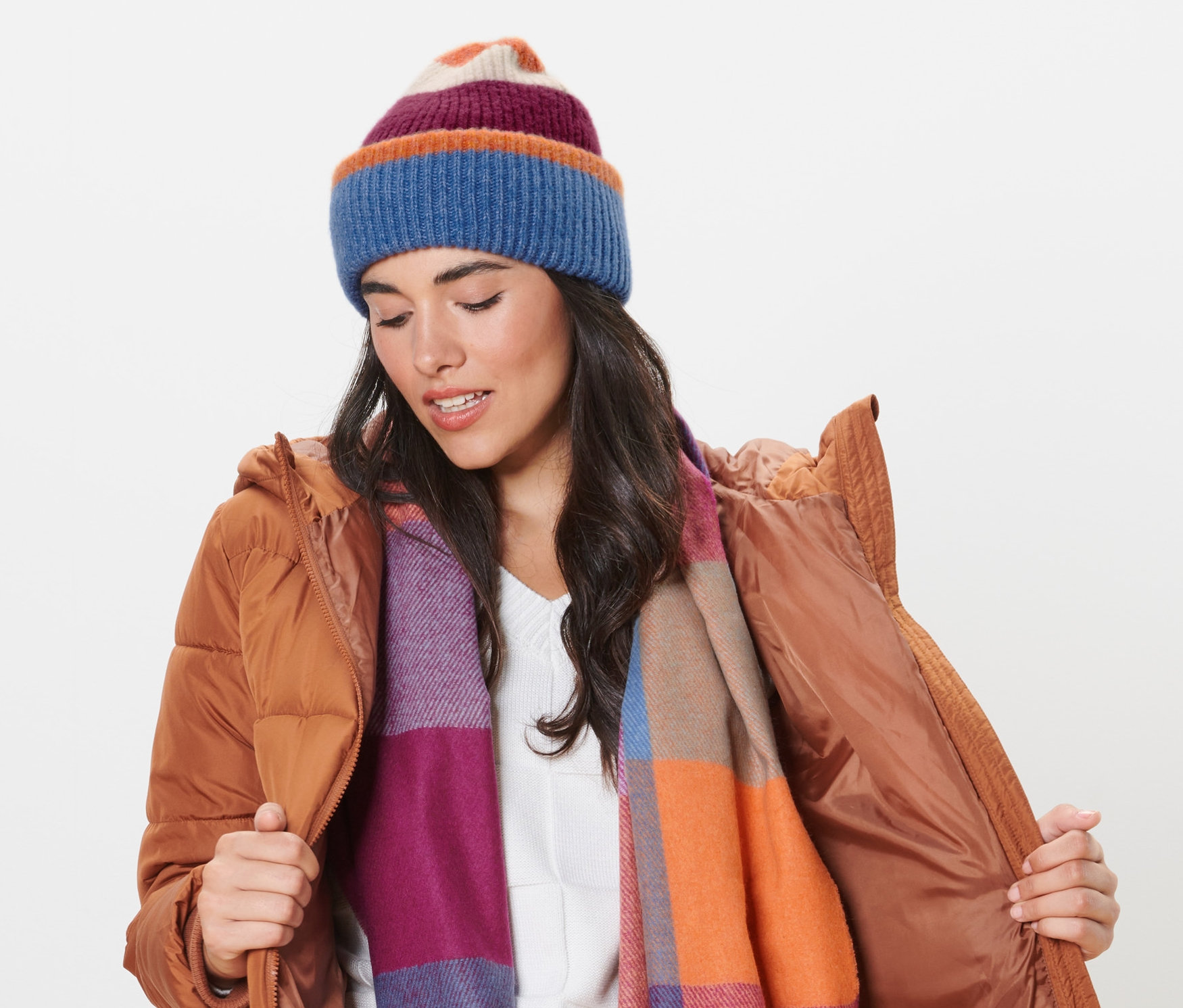 Kobieta w brązowej kurtce poprawia czapkę z dzianiny i nosi szalik.