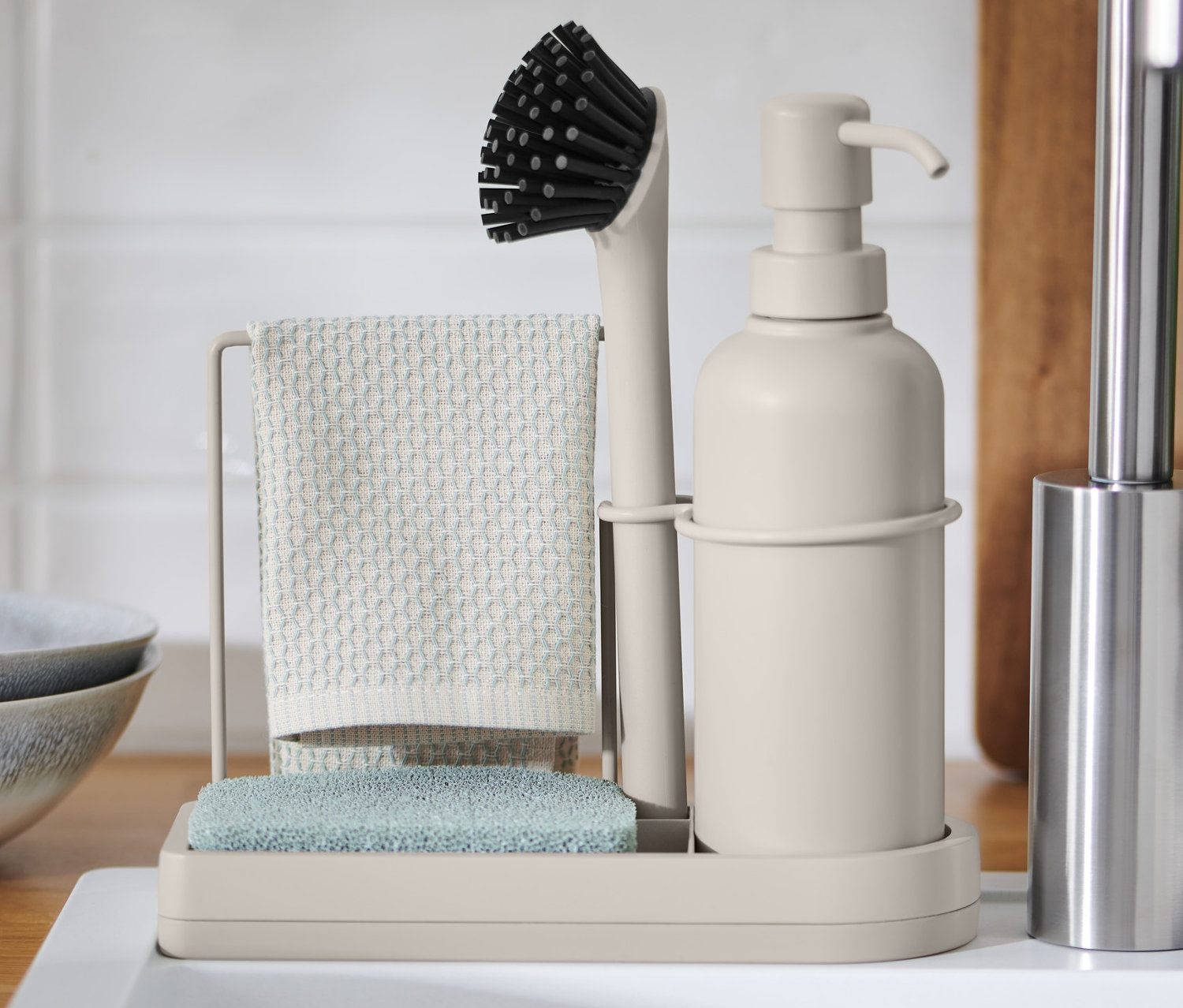 Stojak na przybory do mycia naczyń ze szczotką, ścierką i gąbką na białym zlewie.