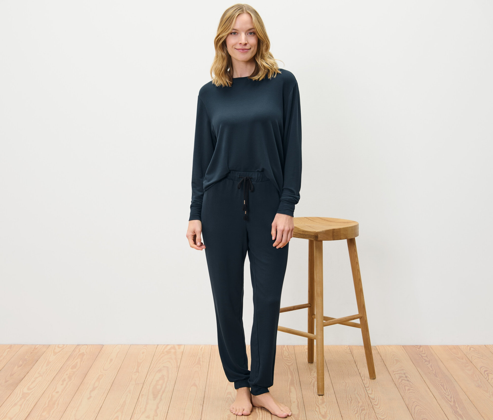 Blondwłosa kobieta stoi i ma na sobie granatowy dres domowy.