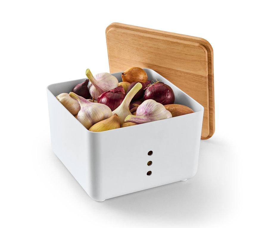 Biały pojemnik do przechowywania wypełniony cebulą i czosnkiem z drewnianą pokrywką opartą o niego.