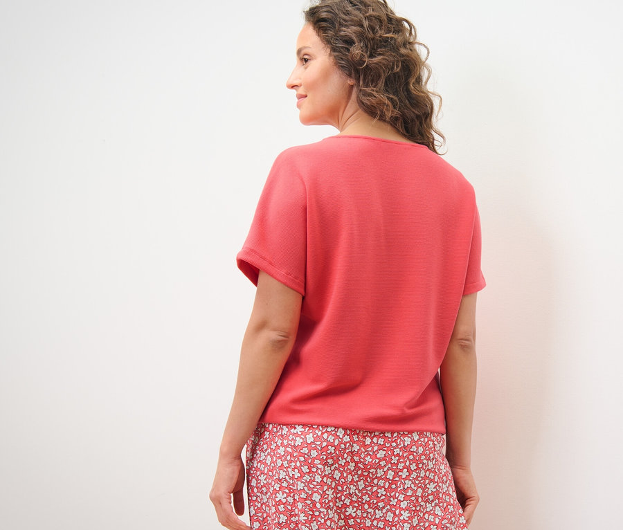 Kobieta spogląda przez ramię, ubrana w koralową bluzkę.