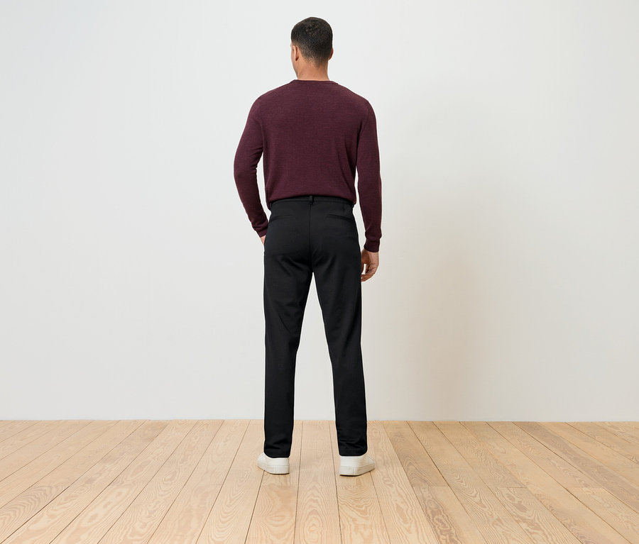 Mężczyzna tyłem do kamery ma na sobie bordowy sweter i czarne spodnie.