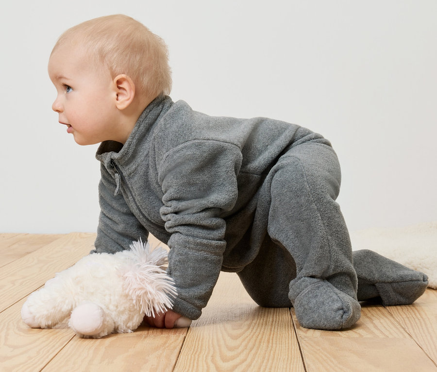 Niemowlę w polarowym pajacyku leży na brzuchu obok pluszowej zabawki.