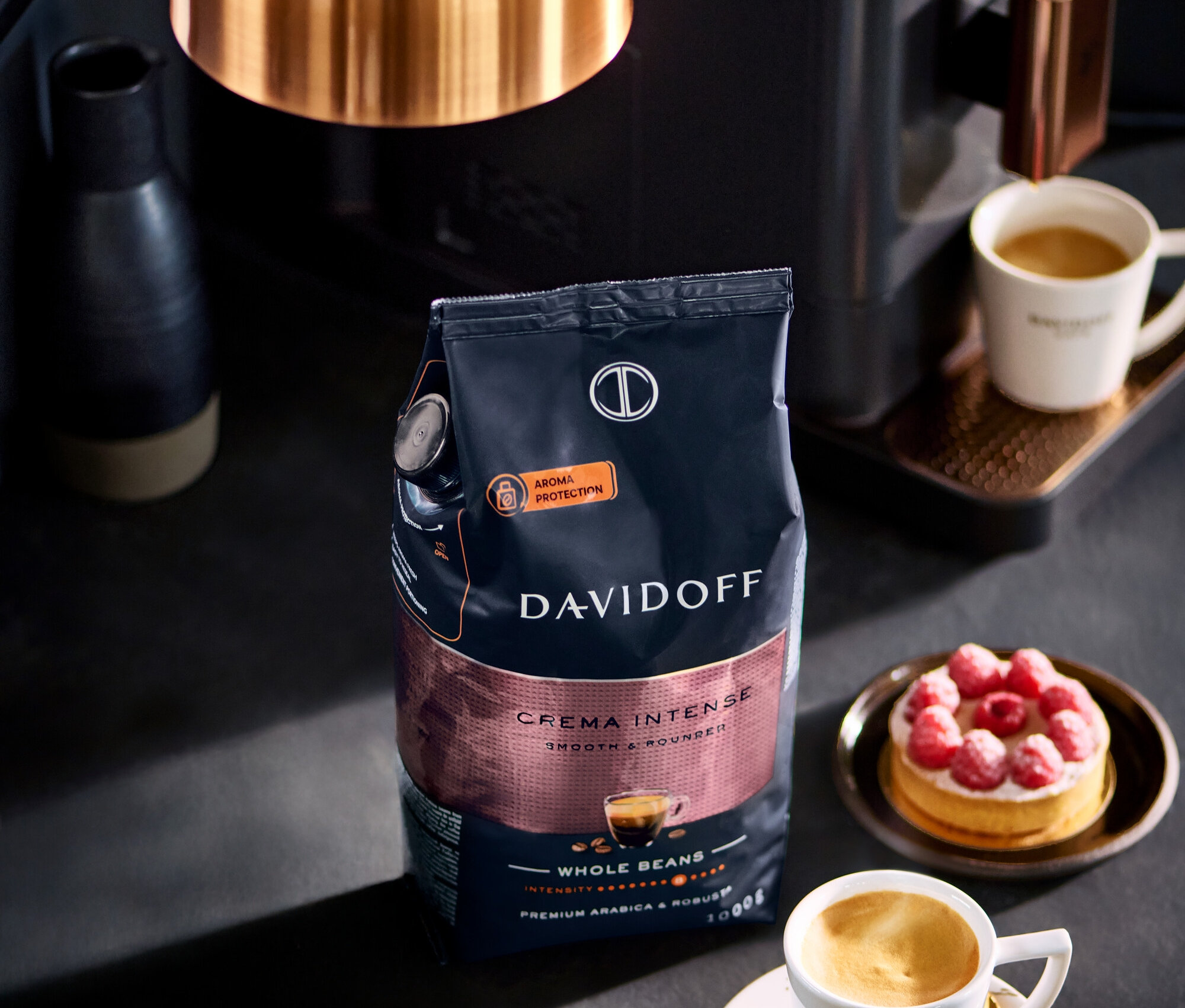 Opakowanie DAVIDOFF CAFÉ Crema Intense 1000 g ziarna stoi obok filiżanki kawy i ciasta malinowego.