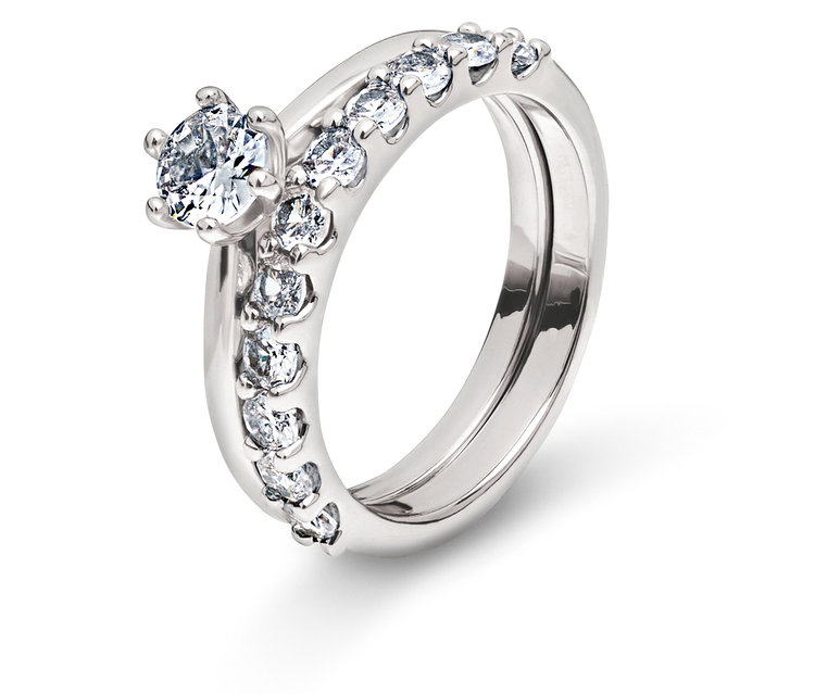 Dwa srebrne pierścionki z przezroczystymi kamieniami na białym tle.