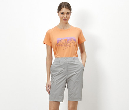 Kobieta stojąca na białym tle ma na sobie pomarańczowy T-shirt z ilustracją gór i szare szorty rowerowo-trekkingowe „Pro”.