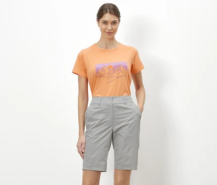 Kobieta stojąca na białym tle ma na sobie pomarańczowy T-shirt z ilustracją gór i szare szorty rowerowo-trekkingowe „Pro”.