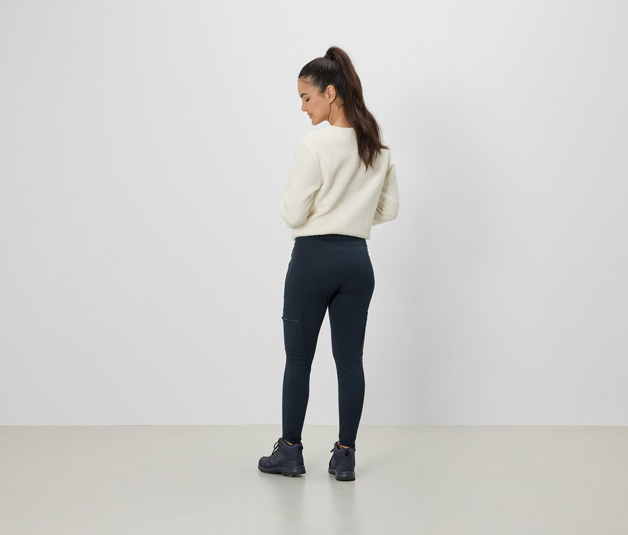 Kobieta w kremowym swetrze i granatowych legginsach z kieszenią, widziana od tyłu.