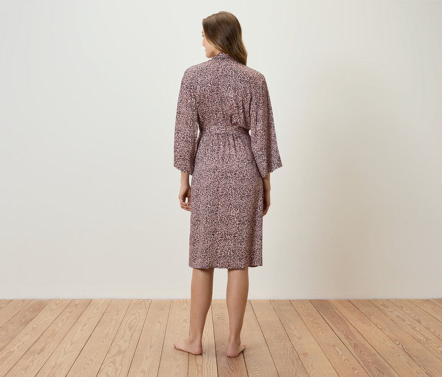 Kobieta stoi tyłem do kamery, ubrana w różowy szlafrok w wzory.