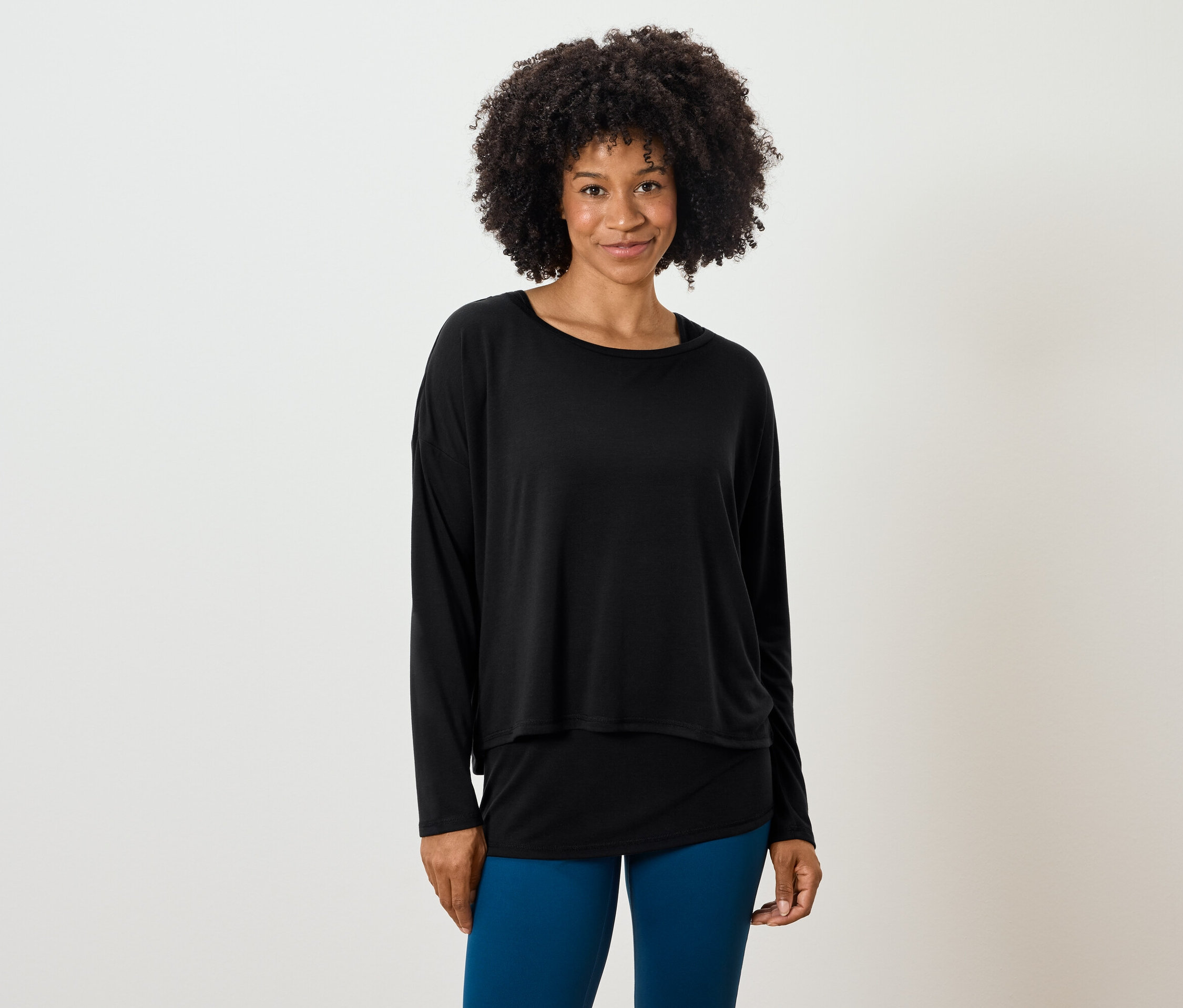 Kobieta z fryzurą afro pozuje w czarnym topie z długim rękawem i niebieskich legginsach.