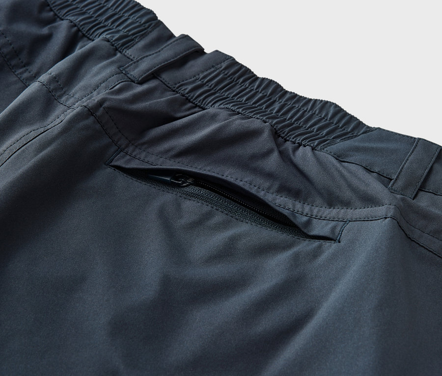 Zbliżenie na granatowe spodnie funkcyjne 2 w 1 z elastycznym pasem i kieszenią na zamek.