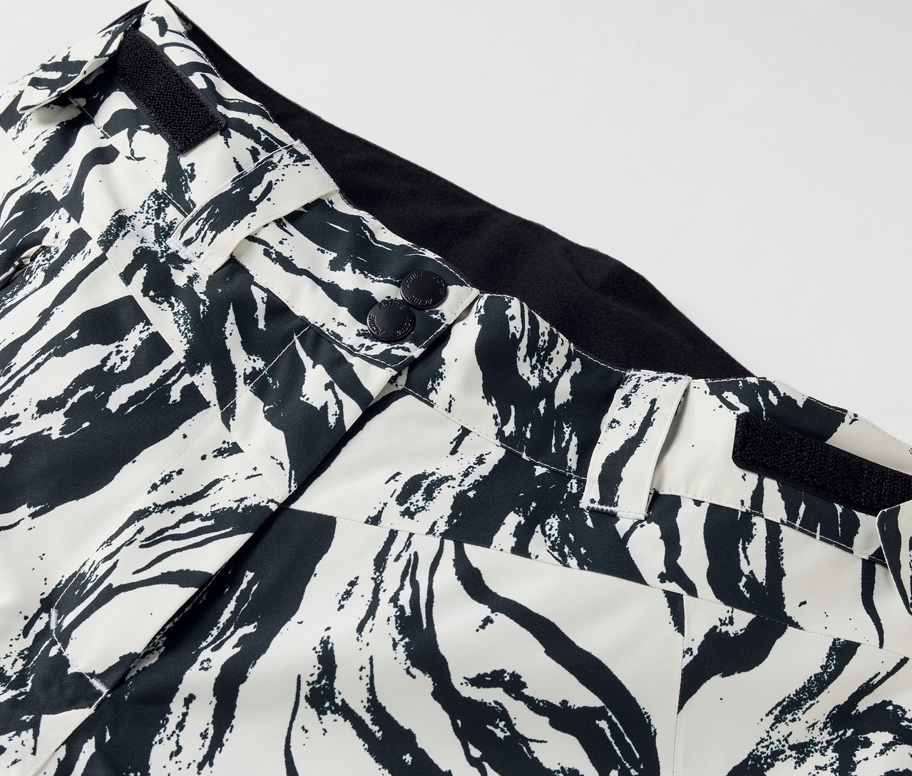 Szczegół spodni we wzór czarno-biały, zapinane na guziki, z czarnym pasem.