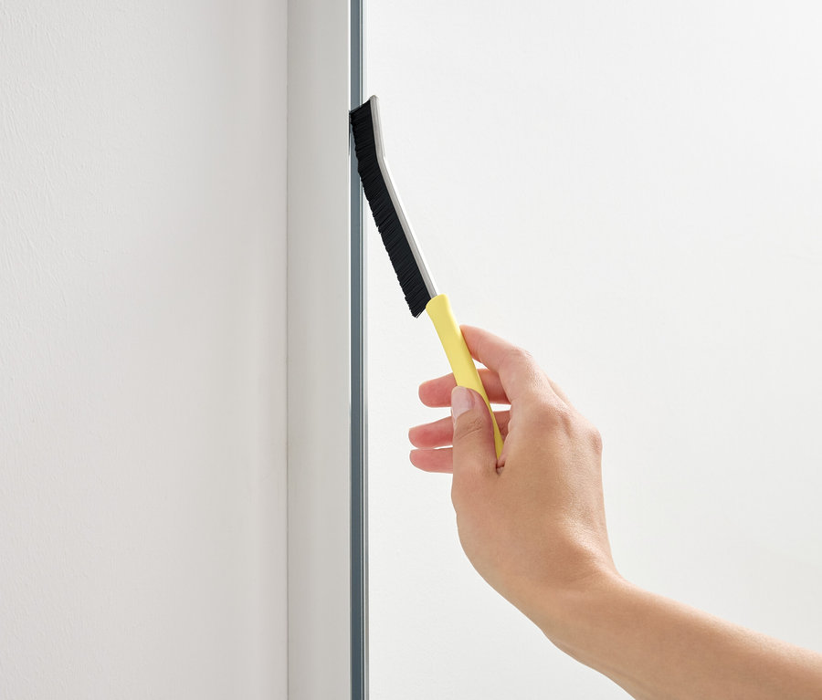 Ręka używa ściągaczki z żółtą rączką na szklanej powierzchni.