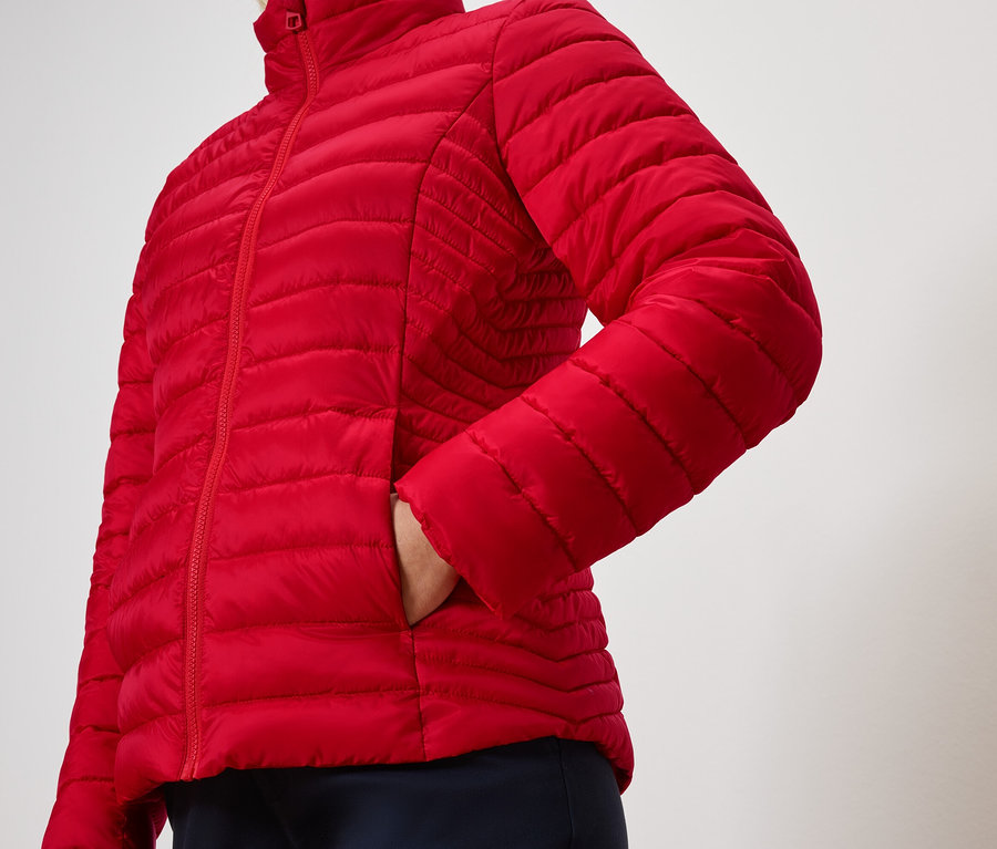 Osoba trzyma rękę w kieszeni czerwonej pikowanej kurtki.