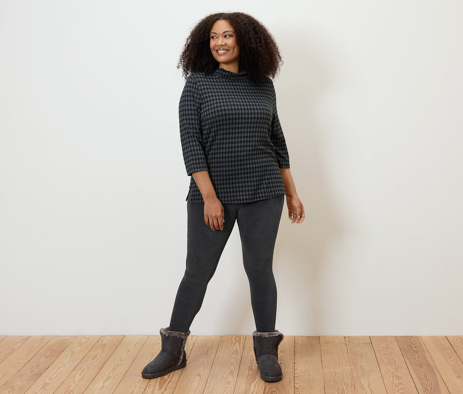 Kobieta pozuje w czarnych sztruksowych legginsach, wzorzystym topie i botkach.