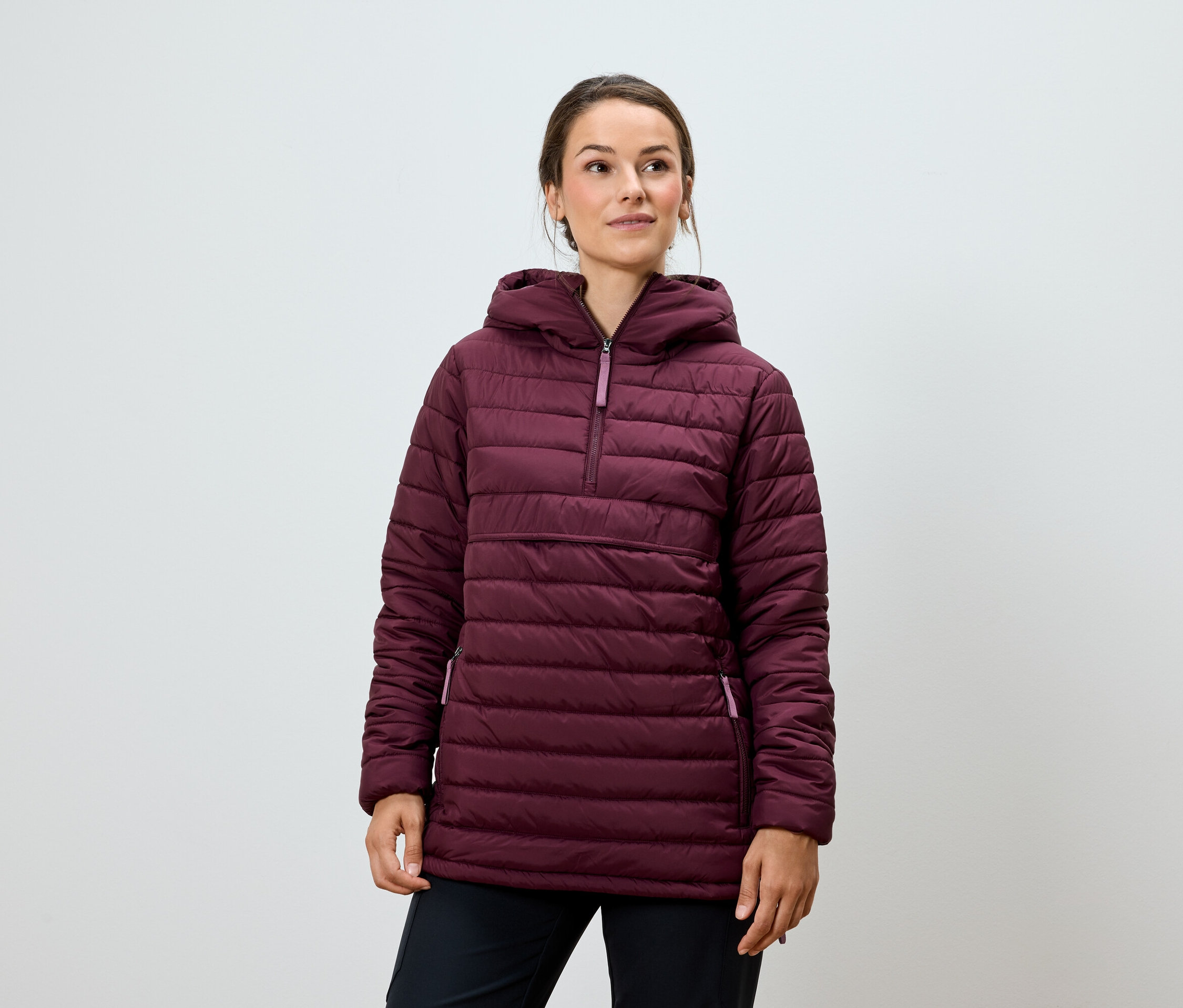 Kobieta pozuje w bordowej, pikowanej kurtce z kapturem i czarnych spodniach.