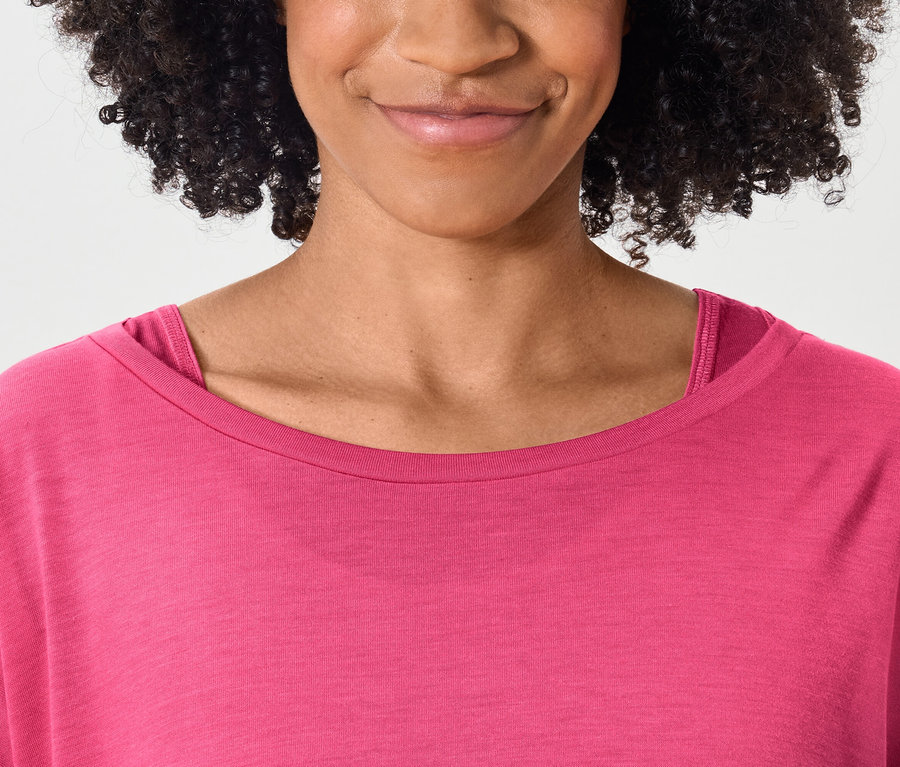 Górna część ciała uśmiechniętej kobiety z ciemnymi kręconymi włosami w różowym t-shircie.