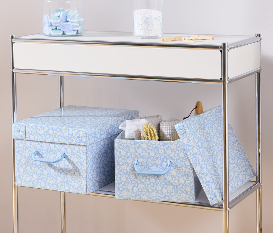 Na półce stoją dwa niebieskie pojemniki do przechowywania z pokrywką i pojemnik do przechowywania z pokrywką z białymi ręcznikami i szczotką w środku.