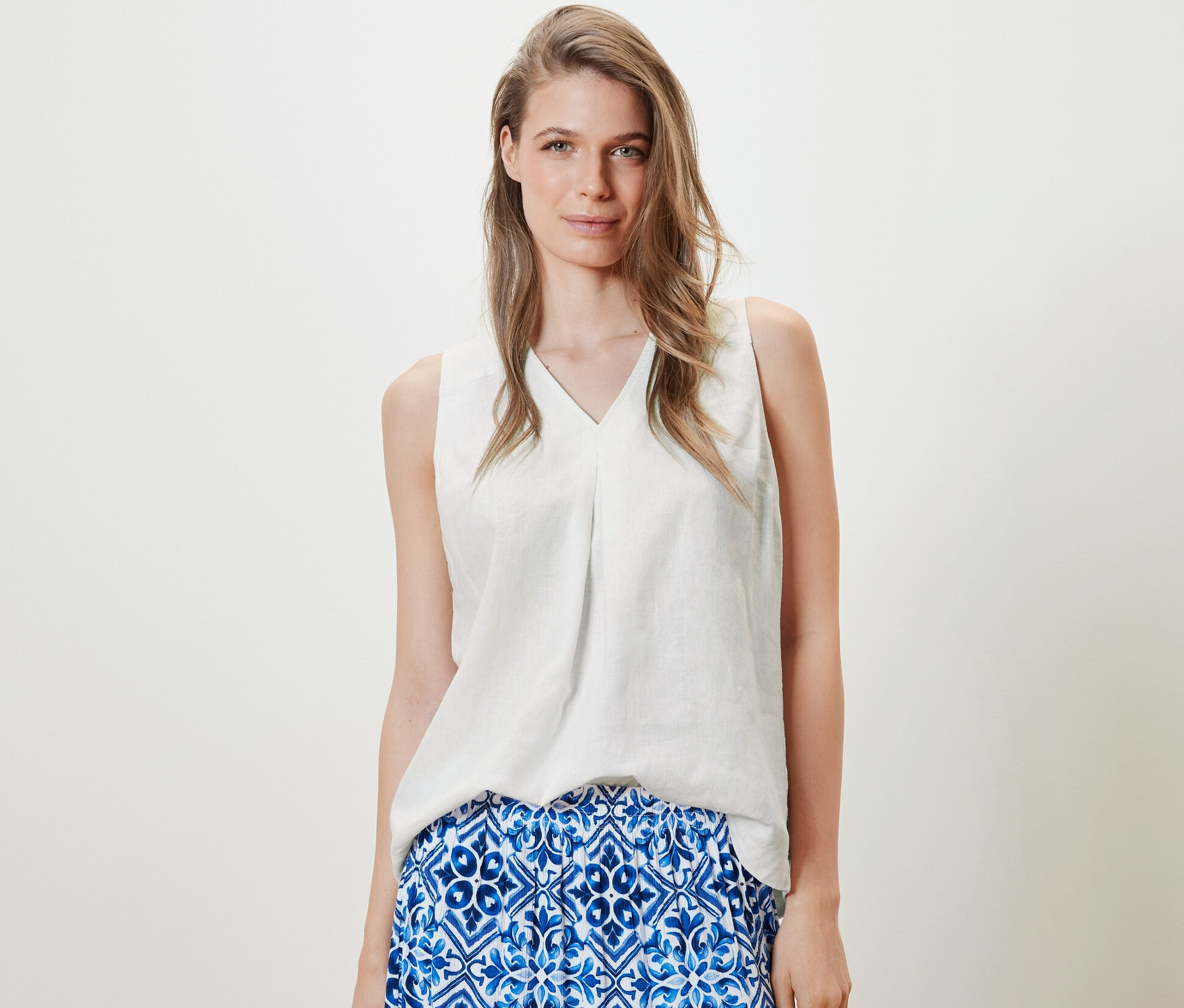 Kobieta ma na sobie białą lnianą bluzkę bez rękawów i niebieską spódnicę.